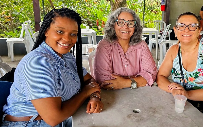 Três mulheres sorrindo à mesa na confraternização da igreja